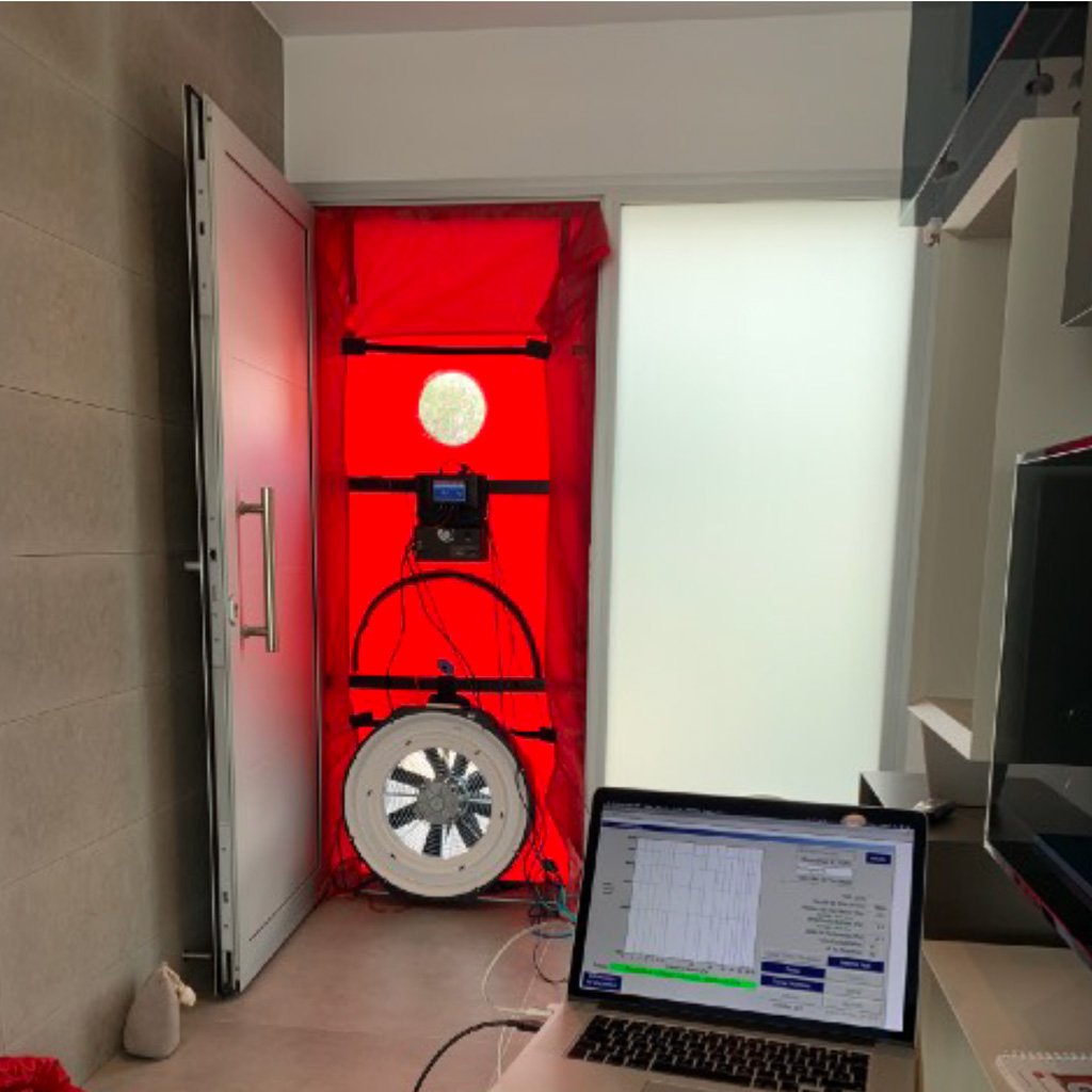 Imagen de una prueba de blower door en una vivienda, mostrando un ventilador montado en una puerta exterior para medir la hermeticidad del edificio. La prueba se utiliza para identificar fugas de aire y mejorar la eficiencia energética del hogar